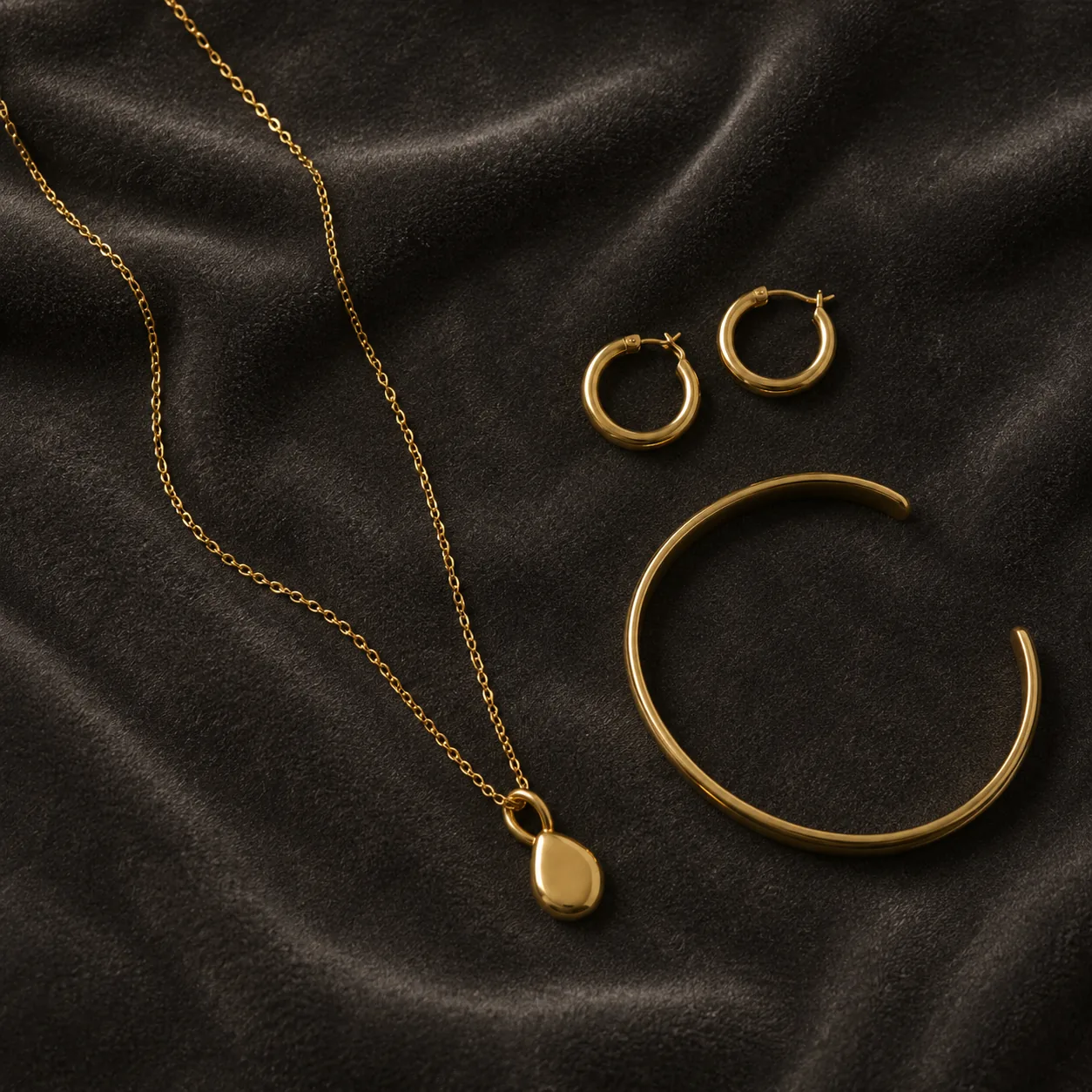 Gold chain necklace, hoop earrings, and bracelet on charcoal velvet
