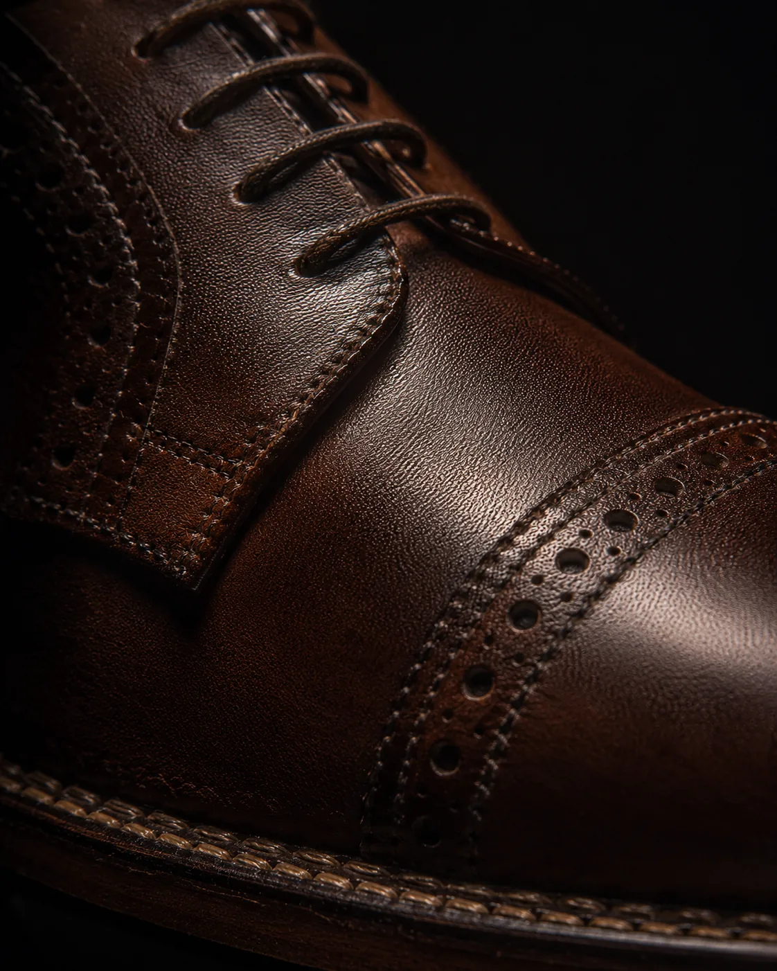 Macro detail of stitching on a leather Oxford, dramatic raking light