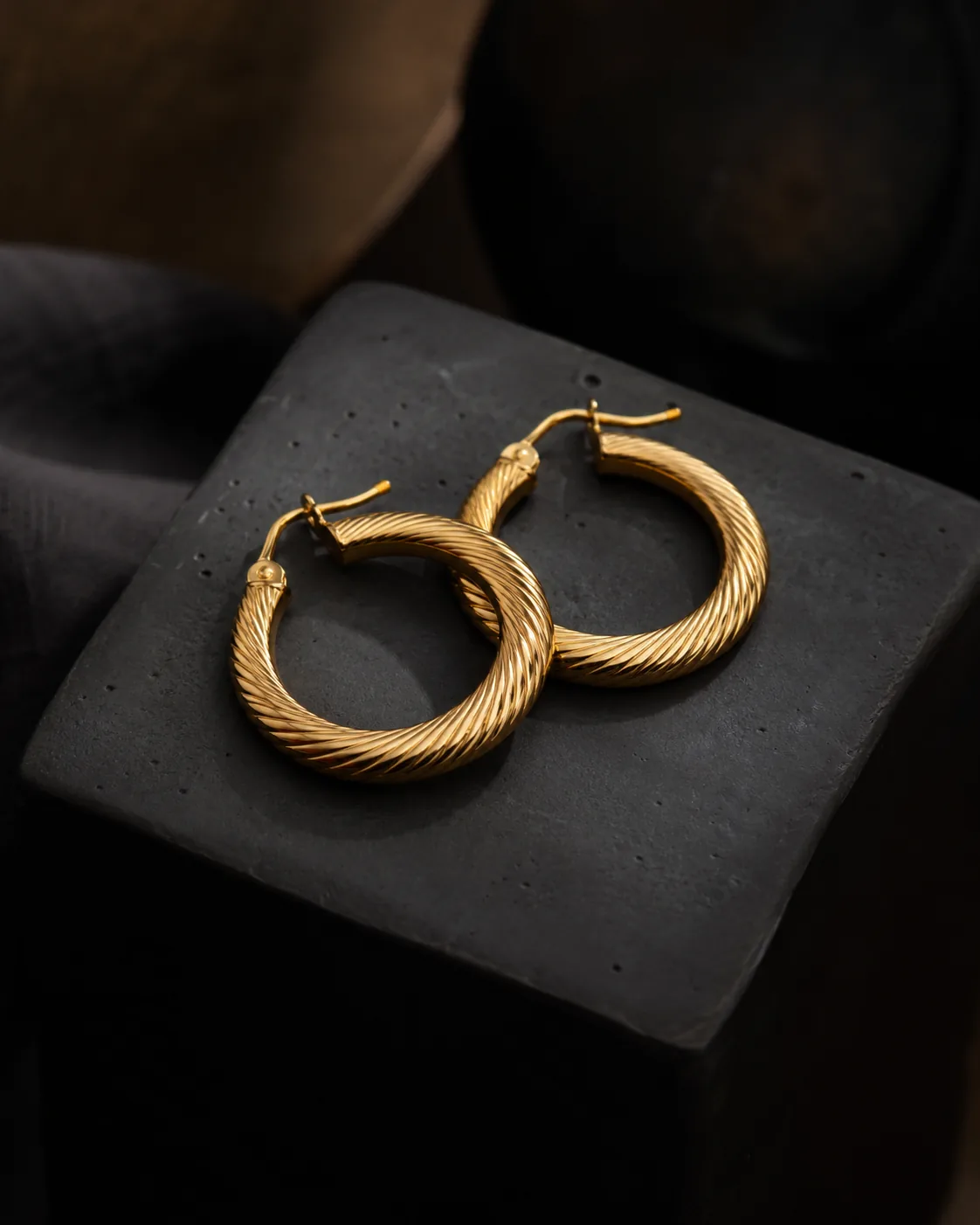 Pair of gold hoop earrings on black ceramic block, macro