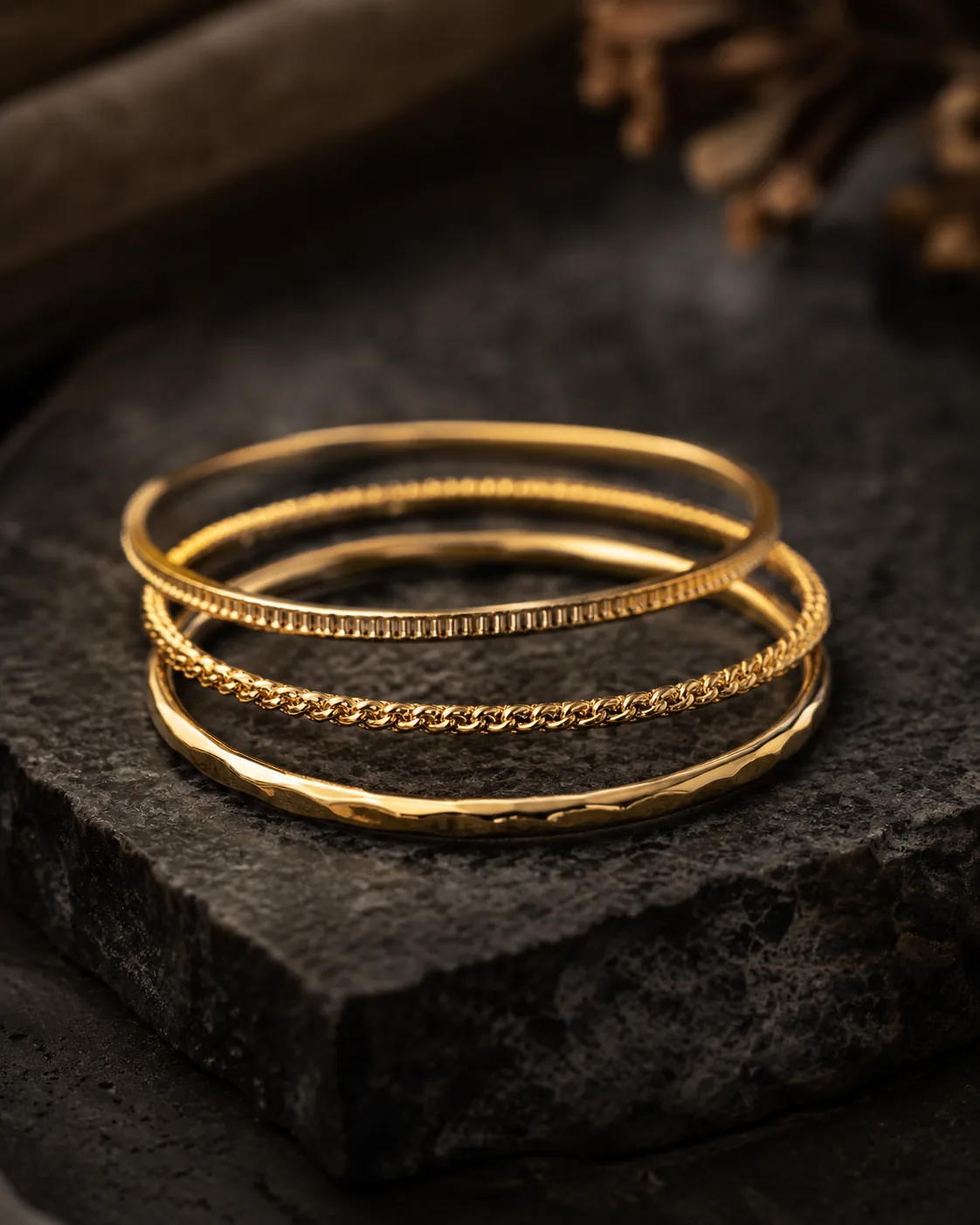 Stack of three slim gold bracelets on charcoal stone surface