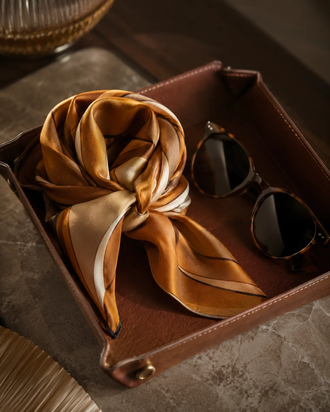 Ochre silk scarf folded with sunglasses on leather valet tray